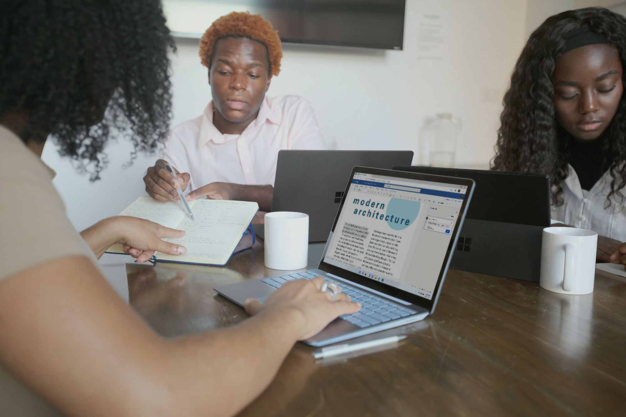 Two black women and a black man disucssing design over a laptop