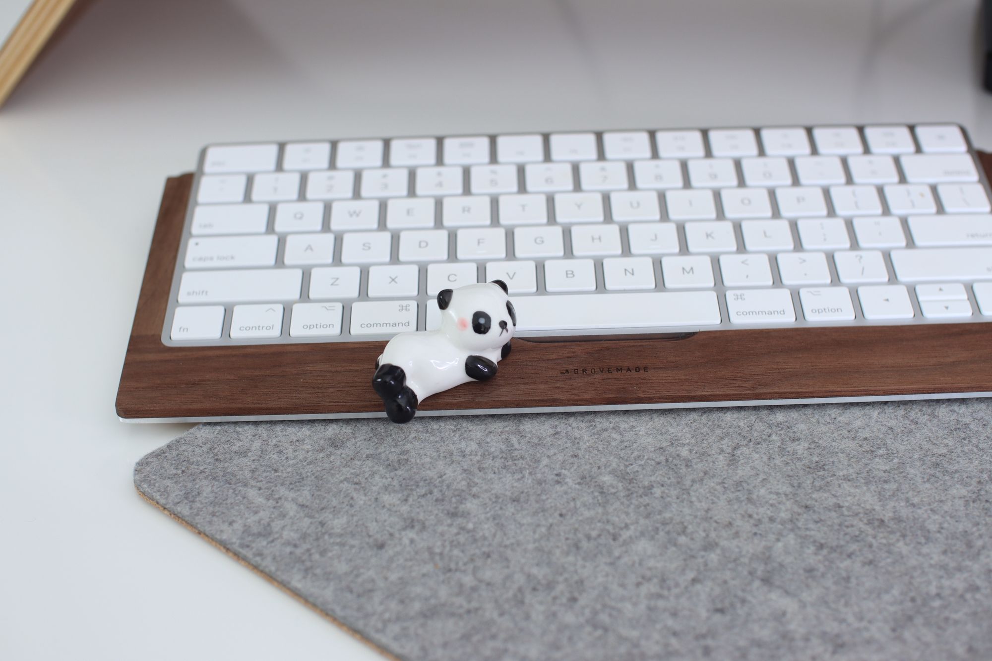 Little ceramic panda sitting on walnut keyboard tray and gray felt mouse