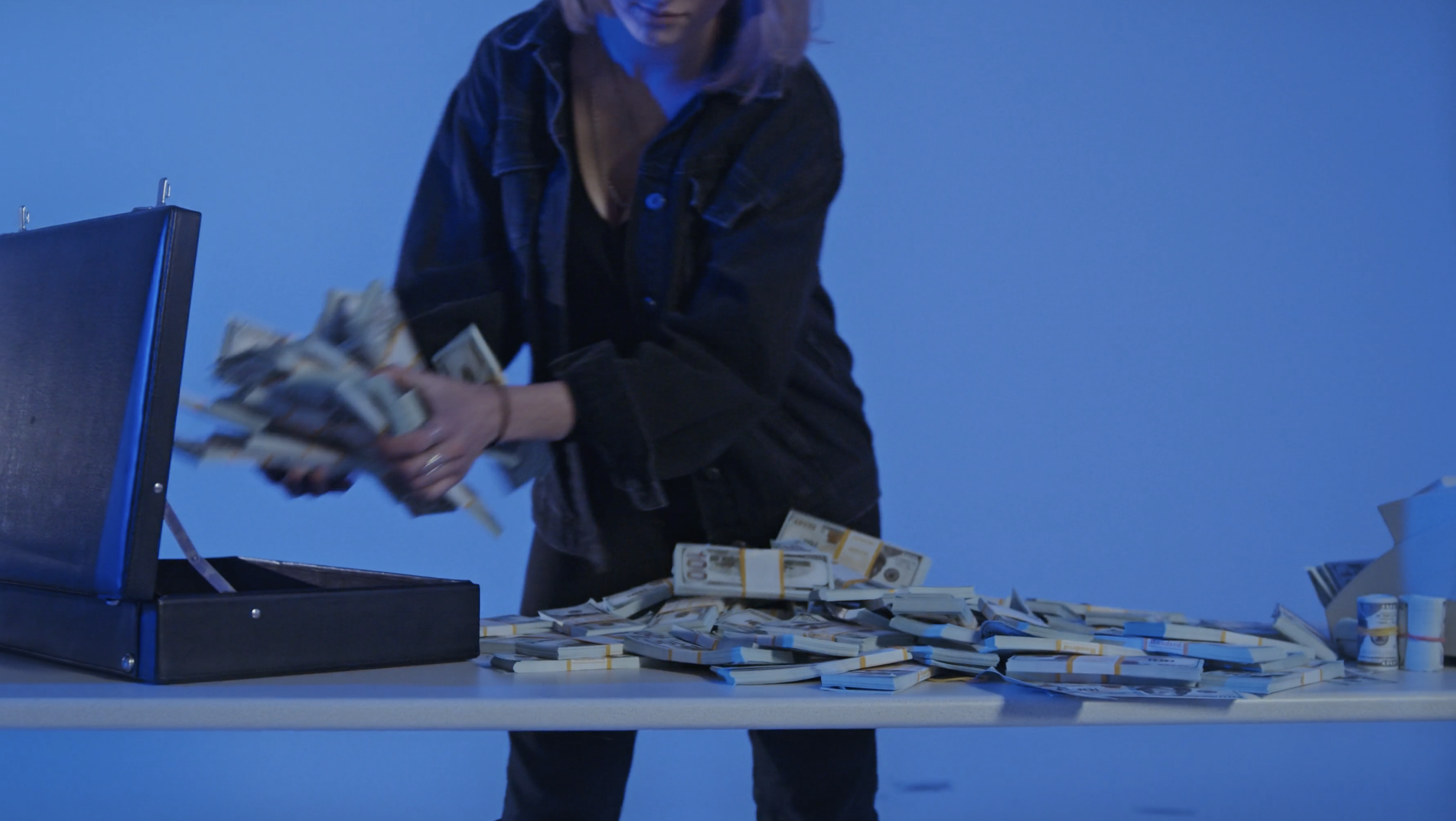 Women wearing black denim jacket and jeans putting stacking of money into a briefcase